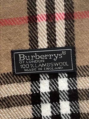 Beige rutig halsduk från Burberrys - Klassisk beige halsduk från Burberrys med ikoniskt rutmönster i svart, vitt och rött. Tillverkad i 100% lammull och har tvinnade fransar i ändarna. Perfekt accessoar för att lyfta din outfit med en tidlös brittisk stil.