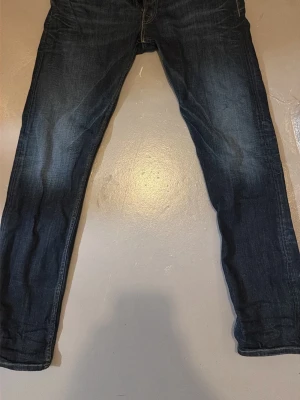 REPLAY NEWBILL mörkblå jeans herr - Säljer ett par mörkblå replay jeans med klassisk femficksdesign och diskreta slitningar. Jeansen har en rak passform som smalnar av vid ankeln och är tillverkade i mjukt bomullsmaterial. Perfekta för dig som gillar en clean och tidlös look.