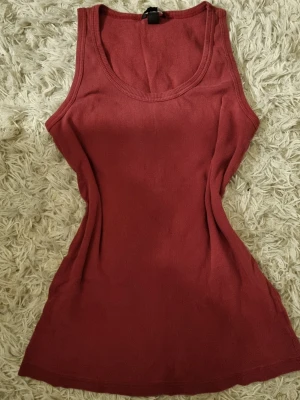 Mörkröd ribbad linnetopp - Snygg mörkröd ribbad linnetopp med rund halsringning och ärmlös design. Perfekt för att matcha med jeans eller kjol för en avslappnad look. Vintage H&M