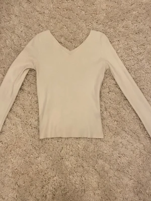 Vit långärmad tröja med v-ringning - En stilren beige långärmad tröja med v-ringad hals. Tröjan är figurnära och har en enkel, klassisk design som passar till många olika outfits. Perfekt för lager-på-lager och går att både klä upp och ner! Den har även väldigt stretchigt och bekvämt material. Köpt utomlands