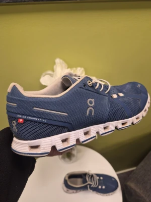 Denim Blåa On Cloud 5 Running sneakers med vit sula - Snygga blå sneakers från On Running med vit, unik sula och meshdetaljer för extra ventilation. Skorna har vita snören och diskreta loggor på sidan. Perfekta för dig som vill ha både stil och komfort i vardagen.