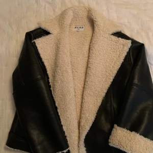 Svart teddyjacka från NA-KD - Säljer en svart teddyjacka från NA-KD med mjukt, krämvitt teddyfoder. Jackan har detaljer i skinnimitation och dragkedja. Varm och skön till vintern🤍knappt använd, xs men passar en s också