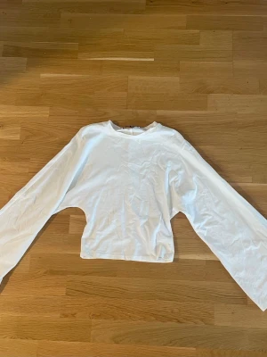 Vit croppad långärmad topp - En enkel och stilren vit croppad topp med långa ärmar och rund halsringning. Tillverkad i mjuk bomull som känns skön mot huden. Perfekt att matcha med jeans eller kjol för en clean look.