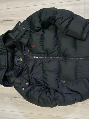 Ralph lauren jacka - Svart pufferjacka från Polo Ralph Lauren för XS. Jackan har ett diskret rött Polo-logo på bröstet och flera praktiska fickor med dragkedja. Perfekt för kalla dagar och har en schysst, klassisk look.