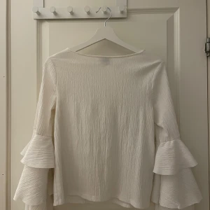 Vit blus med volangärmar  - Säljer en vit blus från Gina Tricot i storlek S. Blusen har en lätt skrynklig struktur och långa ärmar med dubbla volanger ner till. Endast andvänd en gång