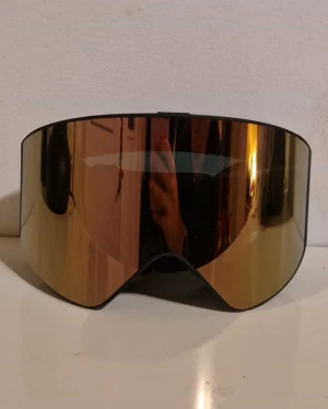Svarta skidglasögon från Dope - Säljer ett par svarta skidglasögon från Dope med bred, spegelblank lins i guldton. Glasögonen har en elastisk svart rem med vit logga och mjuk vaddering på insidan för extra komfort. 