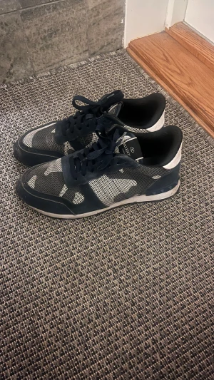 Valentino Rockrunner sneakers blå/vit - Snygga Valentino Rockrunner sneakers i marinblå och vitt med coolt camouflage-mönster. Skorna har snörning, platt sula och meshdetaljer som ger en sportig vibe. Perfekt för dig som gillar streetstyle och exklusiva märken.