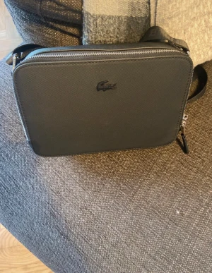 Lacoste väska  - En oanvänd Lacoste väska. Ny skick. Den är riktigt stilren och passar perfekt runt axeln.