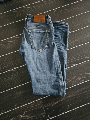  Blåa Tiger of Sweden jeans - Snygga blå jeans från Tiger of sweden med klassisk femficksdesign och raka ben. Jeansen har slitningar och kontrastsömmar, samt en brun t/j-lapp bak i midjan. Perfekt passform och tidlös look som funkar till allt.