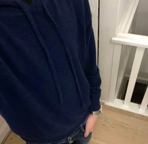 Mörkblå Kashmir Hoodie - Mörkblå hoodie från S&T Studios med huva och snörning. Tröjan är i kashmir och har långärmade ärmar. Perfekt för dig som gillar en chill och enkel stil. Passformen är normal och materialet känns mjukt och skönt mot huden.