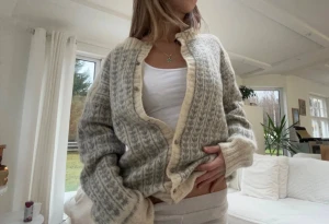 Grå och beige stickad kofta med mönster - Supermysig stickad kofta i grått och beige med ett diskret mönster. Koftan har ribbade muddar, rund hals och knappar framtill. Perfekt att slänga på sig när det är lite kyligt och passar till allt från jeans till mjukisbyxor.passar S-M