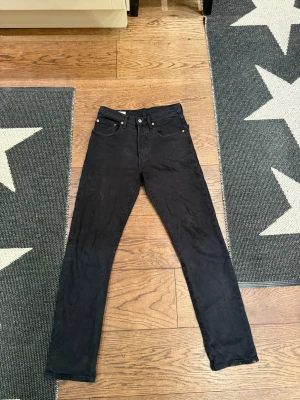 Svarta Levi's 501 jeans straight fit - Svarta Levi's 501 jeans med klassisk straight fit och fem fickor. Jeansen har knappgylf, silverfärgade nitar och Levi's röda logotagg på bakfickan. Materialet är robust denim i bomull, perfekt för en clean och tidlös look. Storlek 25 30, använda max 10 gånger.