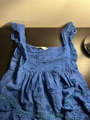 Blå ärmlös topp från MNG - Supersöt blå topp från MNG med broderade blommor och volangdetaljer. Klänningen är ärmlös med breda axelband och har fina spetsinslag och rynkade partier upptill. Perfekt för sommarens alla tillfällen!