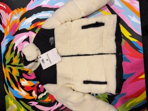 Vit teddyjacka från The North Face - Säljer en fluffig teddyjacka från The North Face i vit färg med svarta detaljer. Jackan har hög krage, dragkedjor på fickorna och framtill samt en oversized passform. Perfekt för kalla dagar och riktigt snygg streetstil.