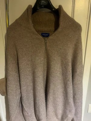 Beige stickad half zip-tröja Jack & Jones - Säljer en beige stickad tröja från Jack & Jones i storlek XXL men passar mer som en XL. Tröjan har en hög krage med ribbad struktur och en snygg half zip-dragkedja framtill. Perfekt för dig som gillar en loose passform och vill ha något mjukt och varmt under hösten och vintern.