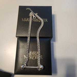 Silverarmband från Maria Nilsdotter - Snyggt silverarmband från Maria Nilsdotter med grov kedja och cool detalj med en stav och två klot i ändarna. Halsband har justerbar längd och kommer i original ask med guldfärgad ormtryck. Perfekt för dig som gillar statement-smycken med edge.
