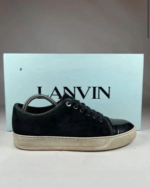 Svarta sneakers från Lanvin i mocka - Svarta sneakers från Lanvin med ovandel i mjuk mocka och blanka skinn-detaljer på tån. Klassisk rund tå, snörning och vit platt sula med diskret struktur. Snygg kontrast mellan material och färg, perfekt för dig som gillar stilrena och lyxiga sneakers. Skriv om ni har frågor eller funderingar!😊