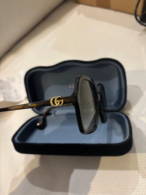 Solglasögon från Gucci - Nypris 3000kr. Kvitto finns. Solglasögon från Gucci. Sidorna har den ikoniska GG-detaljen i guld. Kommer med originalfodral i svart sammet. Perfekta för dig som vill ha en lyxig och trendig look.