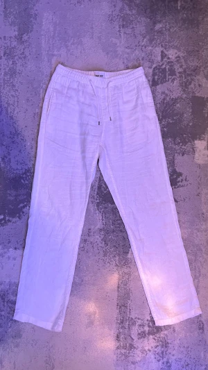 Vita linnebyxor med snörning från East West - Säljer ett par fräscha vita linnebyxor från East West. Byxorna har avslappnad passform, elastisk midja med snörning och raka ben. Perfekta för varma dagar och chill stil. Lätta och luftiga i materialet.