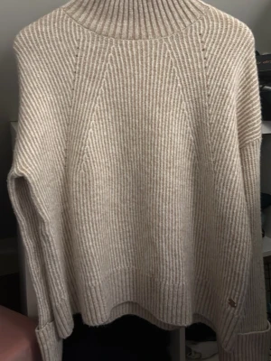 Beige ribbad polotröja Pernilla Wahlgren - Säljer en beige ribbstickad polotröja från Pernilla Wahlgren Design i storlek S. Tröjan har hög polokrage, långärmad modell och en liten metallknapp med ananasdetalj vid mudden. Perfekt för kyliga dagar och har en loose passform.