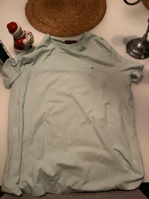 Ljusblå t-shirt från Morris Stockholm - Snygg ljusblå t-shirt från Morris Stockholm med diskret logga broderad på bröstet. Klassisk rund hals och korta ärmar, tillverkad i mjuk bomull som känns skön mot huden. Perfekt för dig som gillar stilrena och enkla plagg. nästan helt oanvänd