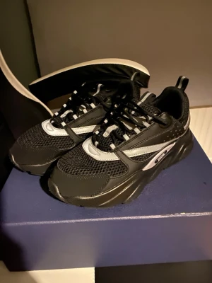 Svarta  sneakers med silvriga detaljer - Säljer ett par snygga sneakers i svart med silvriga detaljer och meshpartier. Skorna har tjock plattformssula, rund tå och snörning. Märket syns tydligt på sidan. Perfekta för dig som gillar exklusiva och trendiga sneakers.