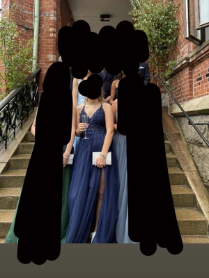 Marinblå balklänning med spets och slits - Säljer en marinblå långklänning med v-ringad spets, tunna axelband och öppen rygg med snörning. Kjolen är i flera lager tyll och har en hög slits framtill. Perfekt för bal eller student! Materialet känns lätt. Använd 2ggr. Köpt på zalando, märke ”mascara”.