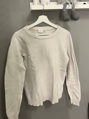 Vit stickad tröja från VILA - Säljer en stilren vit stickad tröja från VILA i storlek M. Tröjan har rund hals, ribbade muddar vid ärmslut och nederkant samt långärmad passform. 