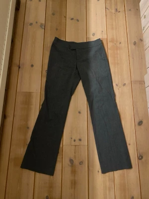 Mörkgrå kostymbyxor från Nelly - Snygga mörkgrå kostymbyxor från Nelly i storlek 38. Byxorna har en rak och klassisk passform med midwaist och är tillverkade i ett mjukt bomullsmaterial. Perfekta för dig som gillar stilrena och enkla plagg med en modern touch. Dem är lite noppriga, men annars finns det inga defekter.