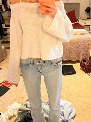 Vit offshoulder stickad tröja - Superfin vit stickad tröja med offshoulder och croppad passform. Tröjan har breda, långa ärmar och ribbad struktur som ger en mysig och trendig look. 