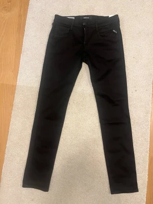 Replay Anbass svarta slim jeans - Svarta Replay Anbass jeans i slim fit med Hyperflex-material som är återanvänt. Klassisk femficksmodell med dragkedja och knapp, stilrena detaljer och snygg passform. Perfekt för dig som gillar stretch och komfort i vardagen.