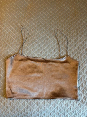 Champagnefärgad satin bandeau topp NLY ONE - Champagnefärgad bandeau topp från NLY ONE i storlek XS. Toppen har tunna axelband och är gjord i ett glansigt satinmaterial som ger en lyxig känsla. Enkel och stilren design, perfekt att matcha med jeans eller kjol.