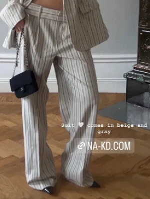 Randig beige kostym från NA-KD - Säljer en snygg randig kostym från NA-KD i beige med tunna svarta ränder. Kavajen har klassisk krage, knappar och fickdetaljer, och byxorna är raka och vida. Perfekt för dig som gillar en stilren och trendig look.