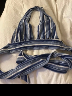 Randig blå och vit linnetopp från SHEIN - Säljer en snygg randig linnetopp från SHEIN i storlek M. Toppen har blå och vita ränder, omlottband som knyts i ryggen och är tillverkad i mjuk ribbad polyester. Perfekt för varma dagar och chill häng med vänner.