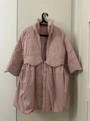 Ljusrosa quiltad jacka - Unik ljusrosa jacka med quiltade cirkelmönster och hög krage. Jackan har trekvartsärmar, knappar framtill och dragkedja upptill. Den har en loose passform och ballongliknande nederdel som ger en cool siluett. Perfekt för dig som vill sticka ut.