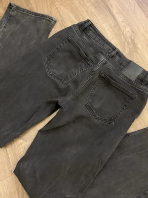 Svarta lågmidjade straight jeans från Lager 157 - Säljer ett par svarta jeans från Lager 157 med klassisk femficksdesign och raka ben. Snygg tvättad look och silverfärgad knapp framtill. Säljer dessa för dem inte kommer till användning. Storlek: waist 27 & lenght 32