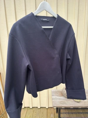 Mörkblå omlottjacka från Gina Tricot - Säljer en mörkblå omlottjacka från Gina Tricot i storlek XS. Koftan har lång ärm, v-ringad hals och dekorativa sömmar längs kanterna. Modellen har en loose passform, perfekt att styla med jeans eller kjol. Fattas en knapp. 