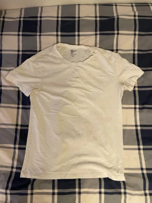 Vit basic t-shirt från H&M - En enkel och stilren vit t-shirt från H&M i storlek M. Modellen är klassisk med rund hals och korta ärmar. Tillverkad i mjuk bomull med stretch för extra komfort. Perfekt att matcha med jeans eller shorts för en clean look.
