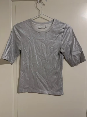 Silver glittrig topp från Kappahl XS - Säljer en snygg silverfärgad topp från Kappahl i storlek XS. Toppen har glittrigt material och rund halsringning med korta ärmar.