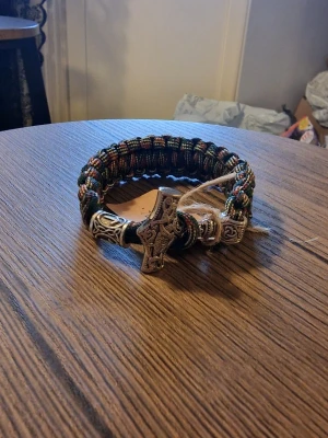 Armband torshammare viking - Säljer ett handgjort armband i brun och beige paracord med en detaljerad Torshammare i metall som lås. Armbandet har grov flätning och coola vikingainspirerade detaljer, perfekt för dig som gillar unika accessoarer. 23,5 cm lång. 3 cm bred.