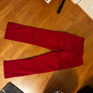 Röda chinos från Polo Ralph Lauren - Snygga röda chinos från Polo Ralph Lauren med raka ben och klassisk passform. Byxorna har sidofickor, bakfickor med knapp och den ikoniska broderade loggan ovanför ena bakfickan. Tillverkade i mjuk bomull med rutigt innerfoder i midjan.