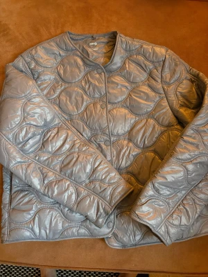 Grå quiltad pufferjacka från MNG MANGO - Säljer en grå pufferjacka från MNG med snyggt quiltat mönster och rundade former. Jackan har knappar framtill och en kort, boxig passform som ger en cool vibe. Perfekt för dig som gillar stilrena och moderna jackor. Storlek XXL men som en normal L