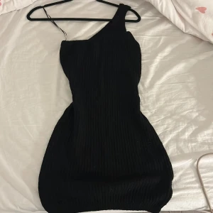 Svart oneshoulder klänning H&M Divided - Säljer en svart ribbad oneshoulder klänning från H&M Divided i storlek S. Klänningen är kort och har en tight passform med snygg asymmetrisk axel. 