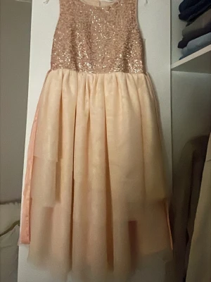Champagnefärgad paljettklänning H&M - Säljer en champagnefärgad klänning från H&M i storlek 140/9-10år. Överdelen är täckt med glittriga paljetter och kjolen är i flera lager med mjukt, skirt tyg. Klänningen har ett satinband i midjan som kan knytas till rosett. Perfekt för dig som gillar lite extra glam.