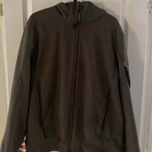 C.P. Company softshell vindjacka grön - Snygg grön softshell vindjacka från C.P. Company med huva och dragkedja framtill. Jackan har två fickor med dragkedja och den ikoniska linsen på ärmen. Tillverkad i stretchigt syntetmaterial för en bekväm passform.           Äkta såklart pris går att diskuteras                             - använd några gånger såklart skulle säga skick 8/10 storlek 54 
