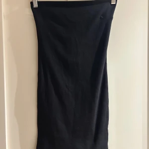 Svart tubklänning med stretch, storlek S - Svart tubklänning i superstretchigt material som sitter tight och följer kroppen. Klänningen är enkel och stilren utan mönster eller detaljer, med rak form och elastisk midja. Perfekt för dig som gillar minimalistisk stil och vill ha en klänning som är lätt att matcha.