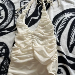 Vit body med öppen rygg  - Helt ny snygg vit body med öppen rygg. Har aldrig använts då den inte passar mig.Bodyn har rynkade detaljer framtill och är tillverkad i ett tunt, mjukt syntetmaterial som ger en cool och trendig look. Perfekt för festens alla kvällar!🤩kom gärna med prisförslag!!