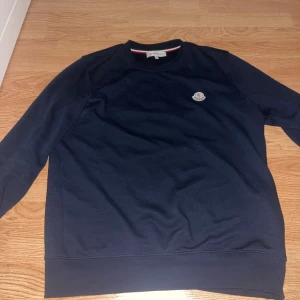 Mörkblå sweatshirt från Moncler - Snygg mörkblå sweatshirt från Moncler med rund hals och diskret logotyp på bröstet. Tröjan har långa ärmar. Perfekt för dig som gillar stilrena och klassiska plagg 