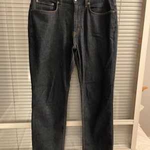 Mörkblå jeans från Spoke, waist 33 - Snygga mörkblå jeans från Spoke i klassisk straight fit med kontrastsömmar. Byxorna är tillverkade av 78% bomull, 20% polyester och 1% elastan, vilket ger en skön och slitstark känsla. Regular passform och fem fickor gör dem både stilrena och praktiska.