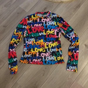 Färgglad långärmad topp med tryck  - Säljer en supercool långärmad topp med färgglatt  tryck där det står 'Love' i olika färger som blå, röd, gul, rosa, orange och grön. Toppen har en rund hals och är figurnära i modellen. Stretchigt material